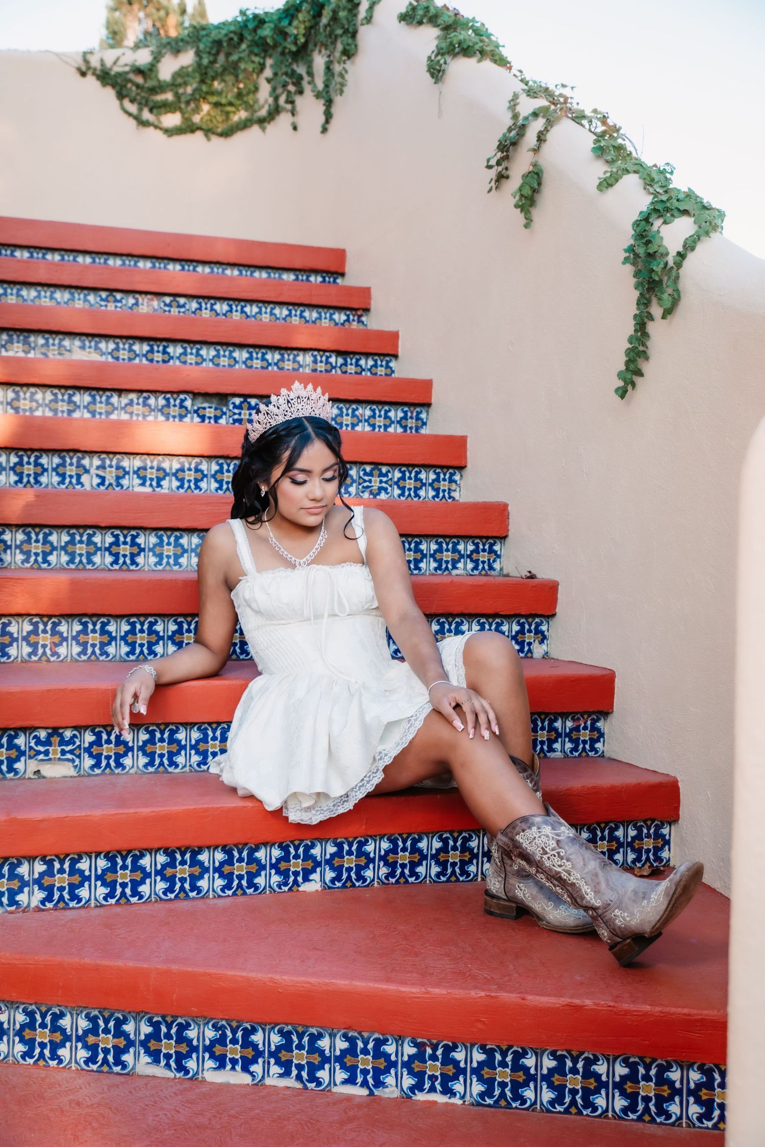 Someone in a white dress reclines on decorative red and blue tiled steps with greenery.