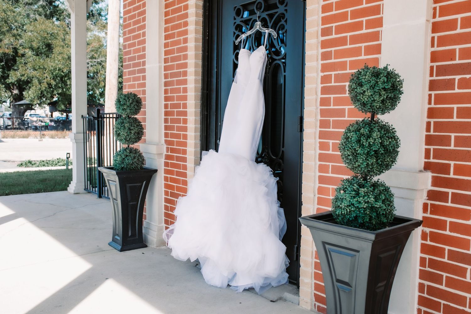 White wedding dress hanging outside brick building with decorative potted plants.