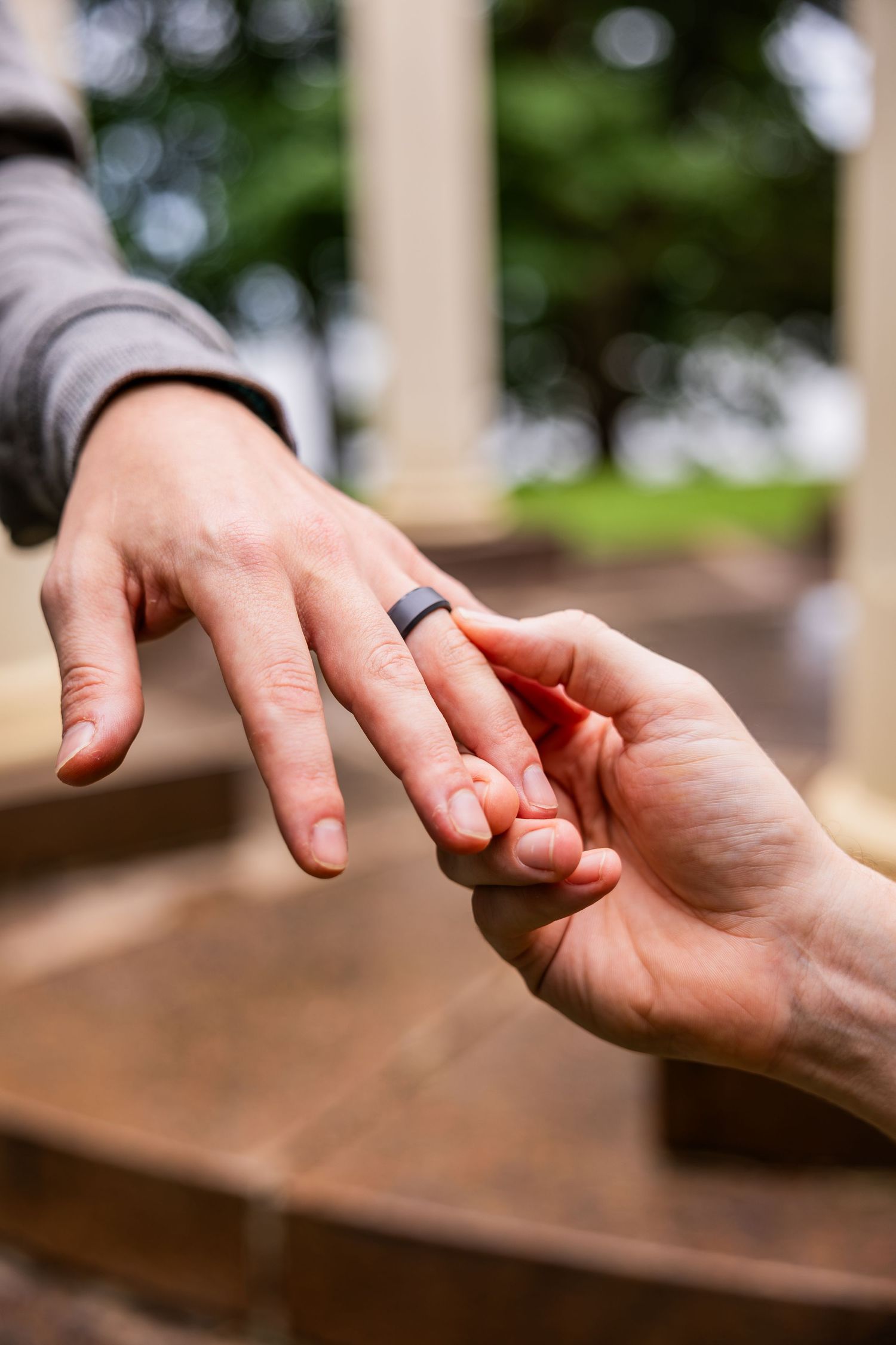 Close-up of hands exchanging a black silicone wedding ring during an outdoor proposal.