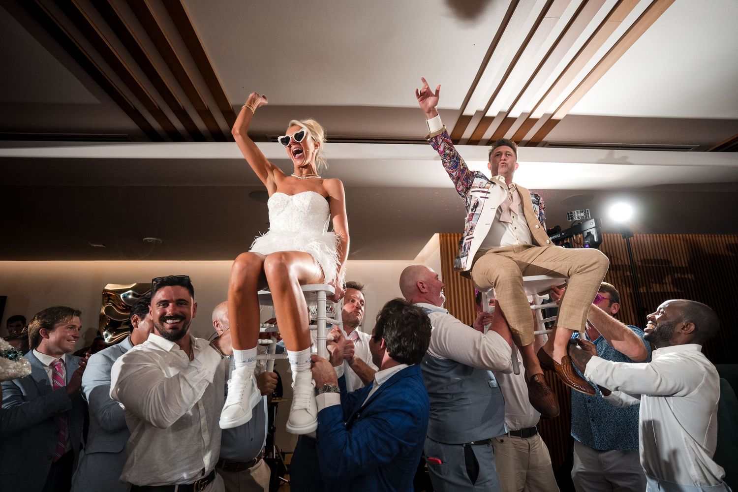 Bride and groom lifted on chairs while guests celebrate at their wedding reception