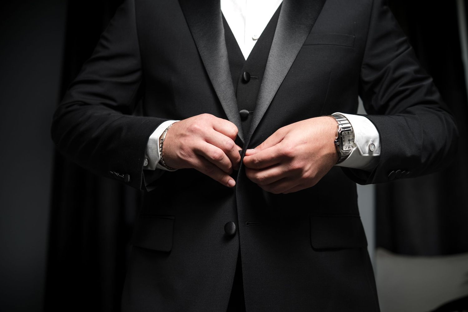 Groom buttoning his black suit during wedding preparations