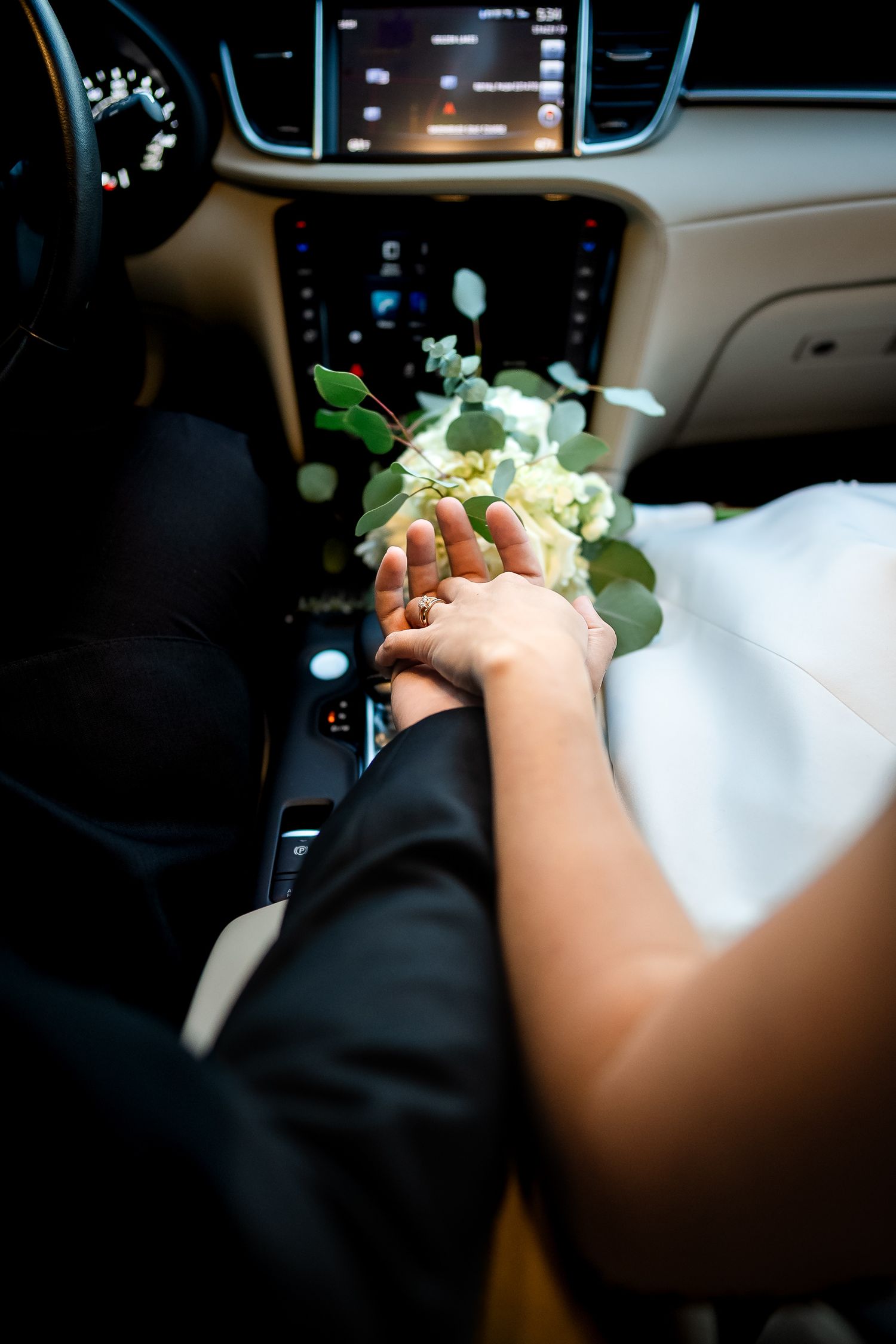 Newlyweds holding hands beside a wedding bouquet inside a car after their Florida wedding