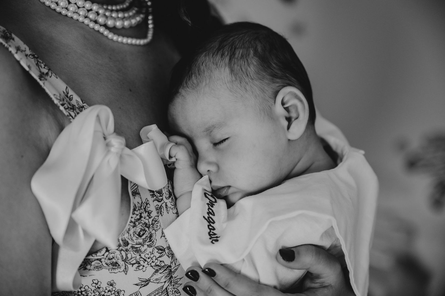 Black and white photo of a sleeping newborn baby cradled against mother with floral dress.