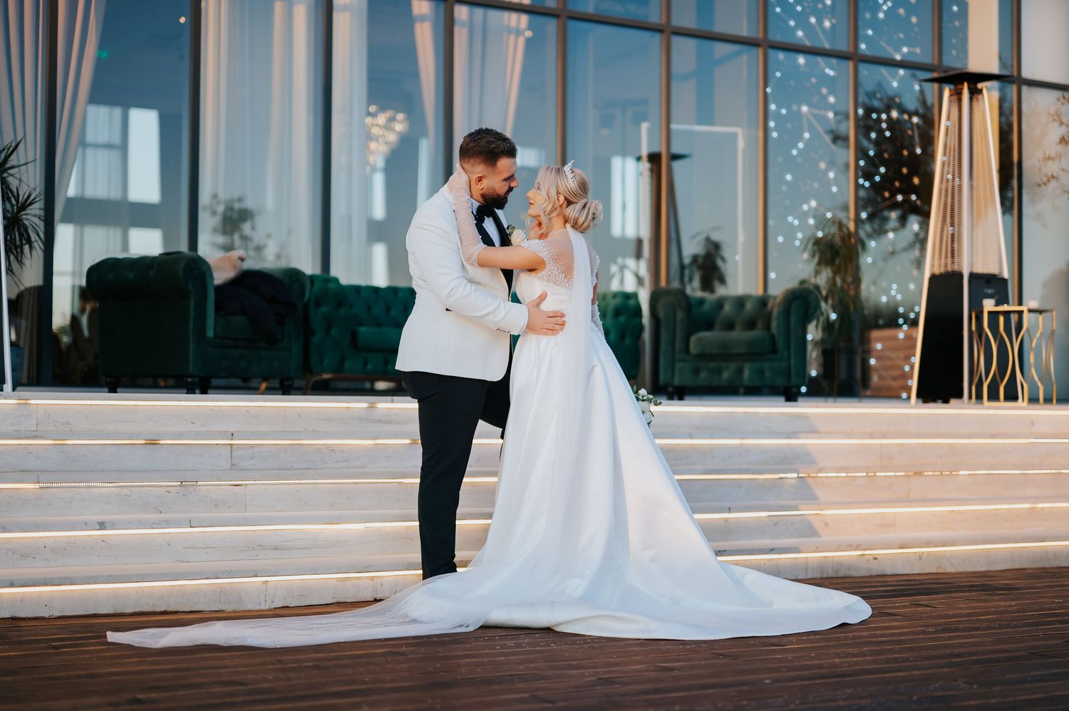 Bride and groom share romantic embrace outdoors at elegant wedding venue with twinkling lights.