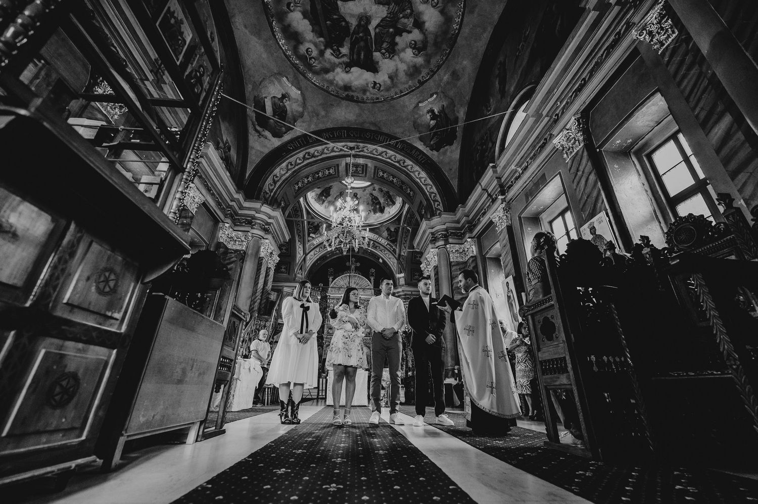 Black and white photo of a wedding ceremony inside an ornate church with painted ceilings and chandelier.