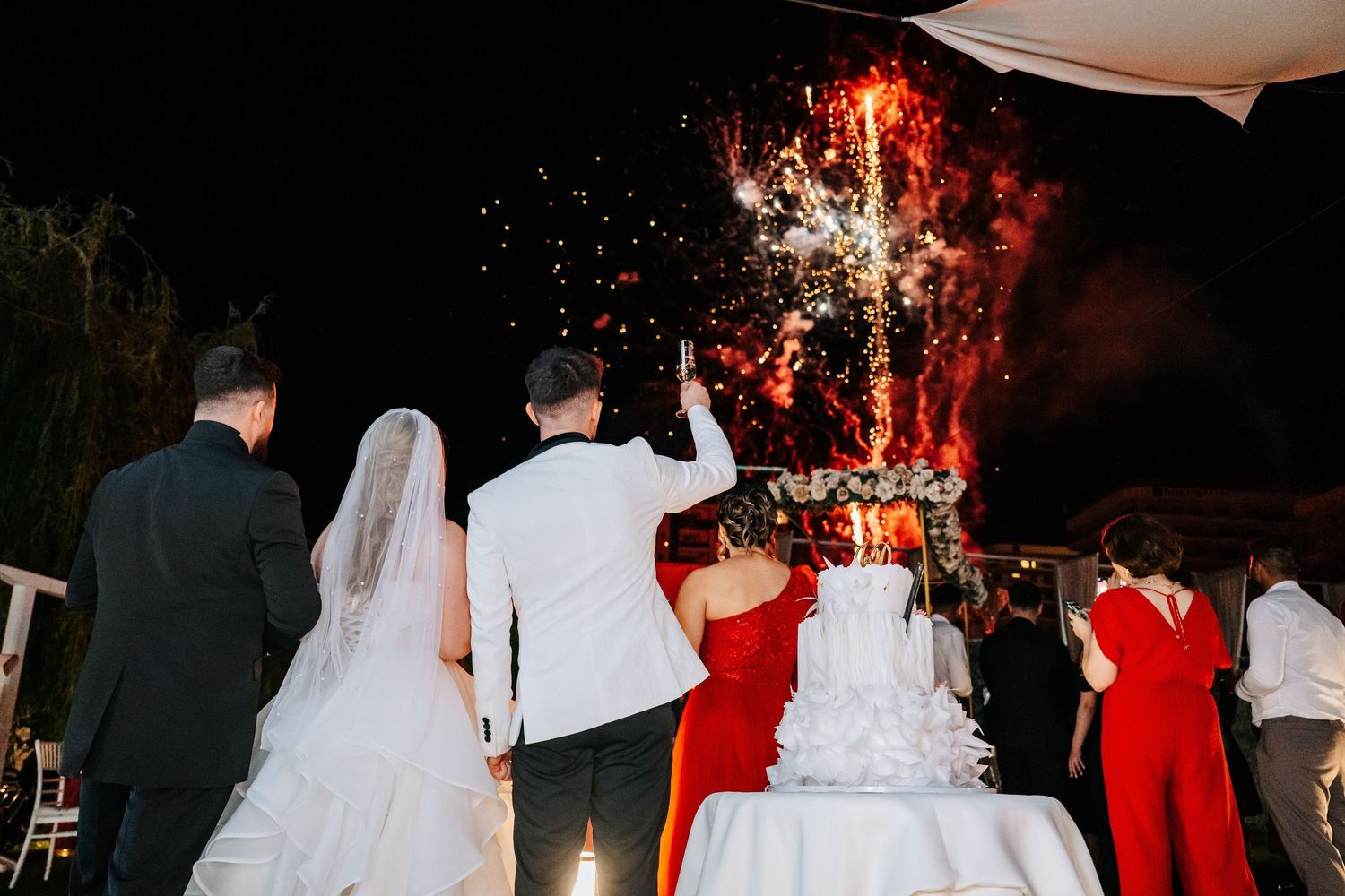 Bride and groom cutting wedding cake with sparklers at outdoor night reception celebration.