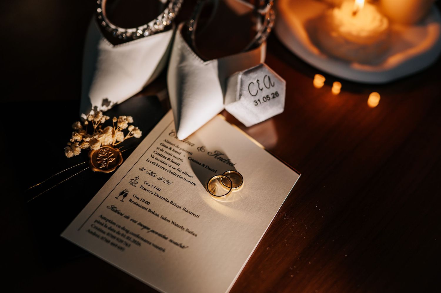 Wedding flat lay with gold ring, invitation card, bridal shoes, and candlelight.