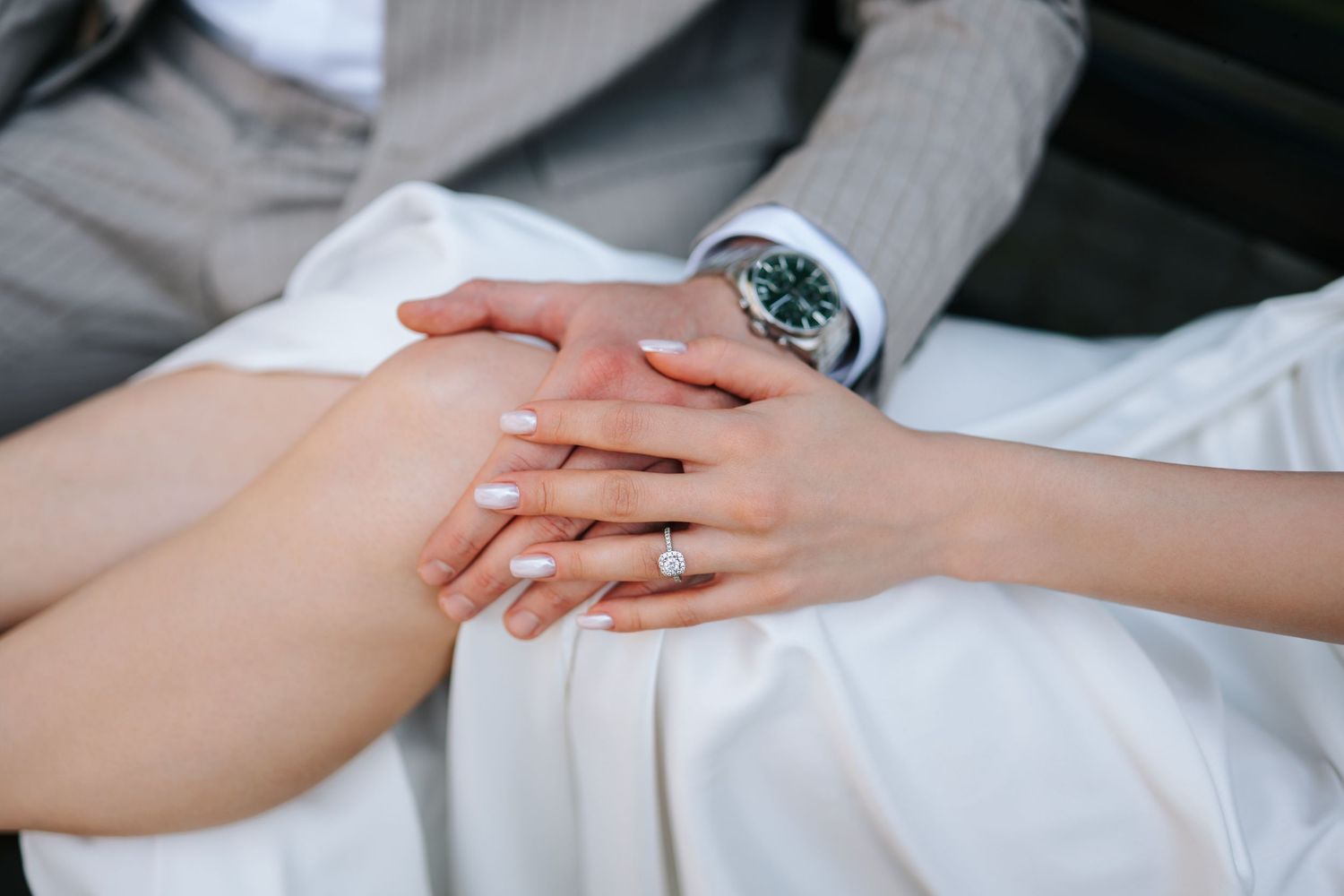 Close-up of bride and groom holding hands showing wedding ring and luxury watch on wedding day.