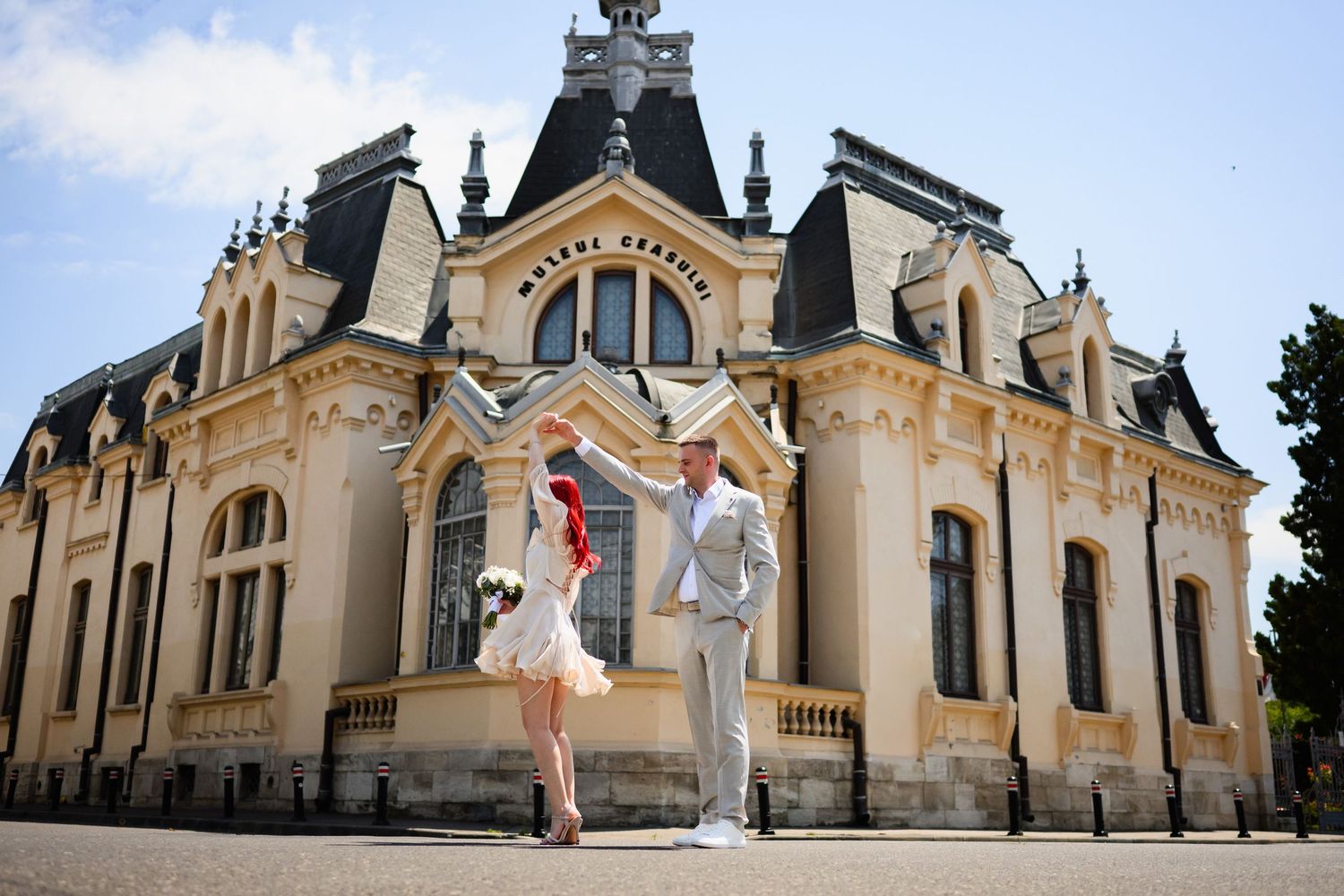 Newlywed couple dancing in front of an ornate historic mansion on a sunny day.