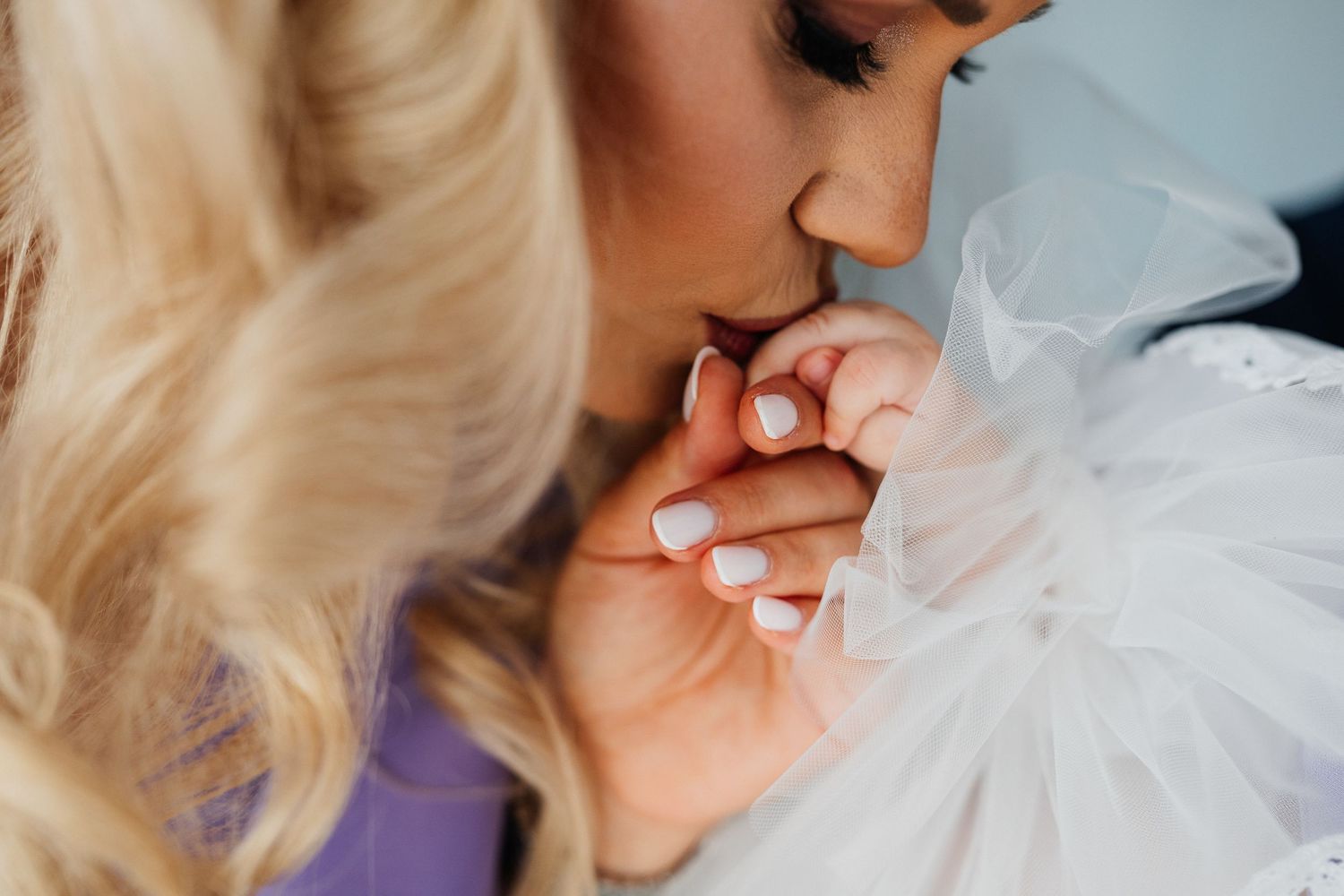 Bride with blonde hair kisses hands of someone in a white tulle dress on her wedding day.