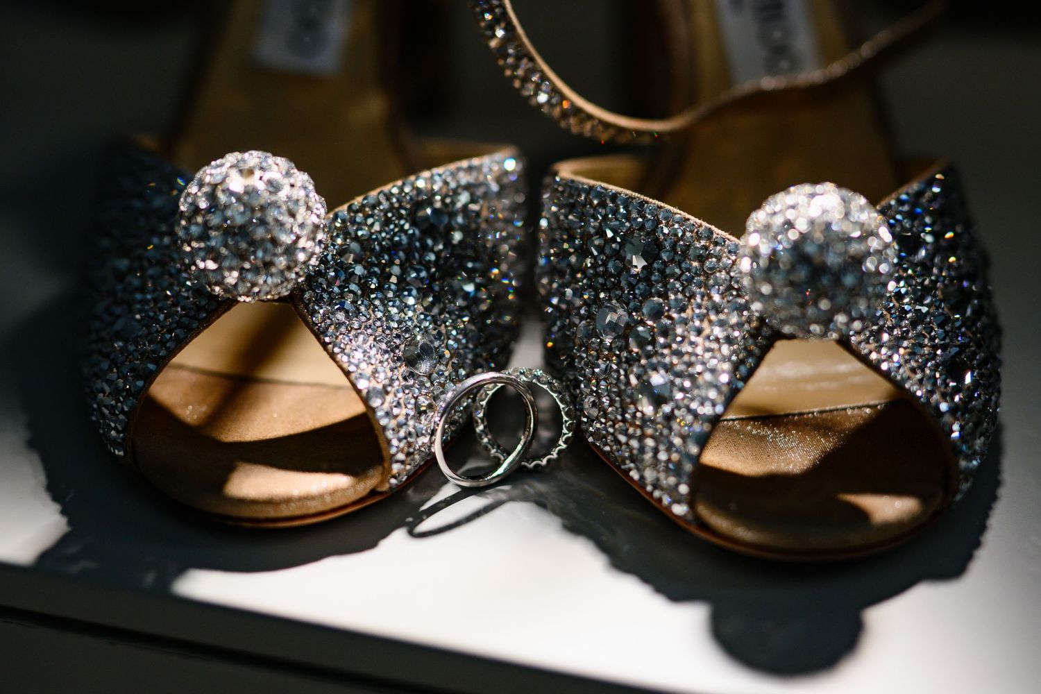 Sparkling crystal-embellished wedding heels with diamond rings placed between the shoes.