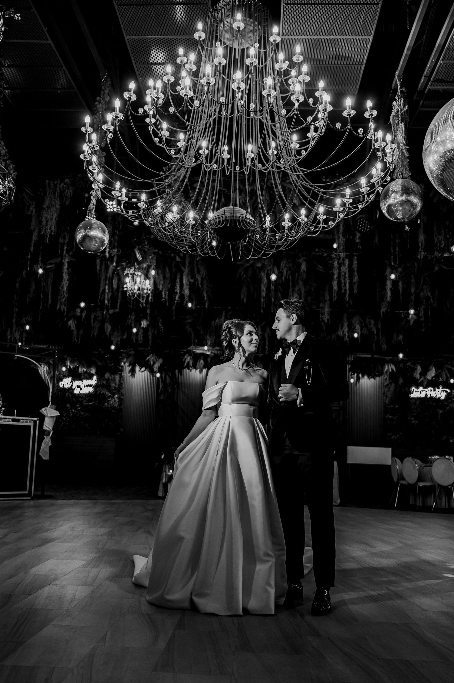 Bride and groom sharing a romantic dance under elegant chandeliers in black and white.