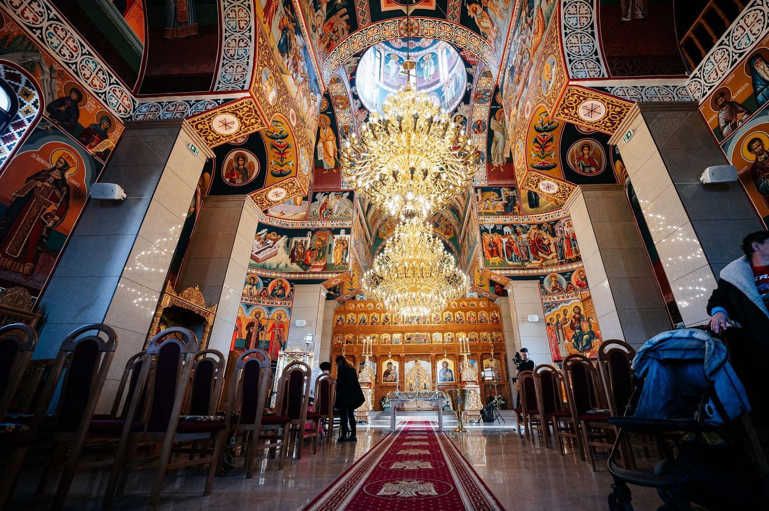 Ornate Orthodox church interior with golden chandelier, vibrant frescoes, and iconostasis under a decorated dome.