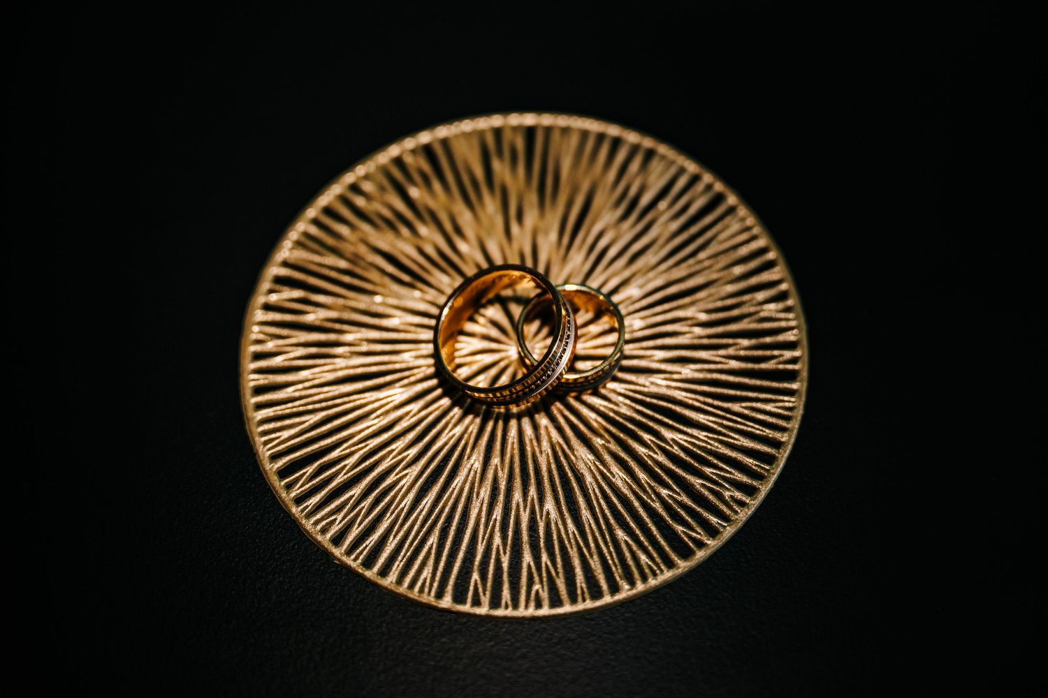 Two gold wedding rings resting on an ornate golden sunburst decorative dish against a dark background.