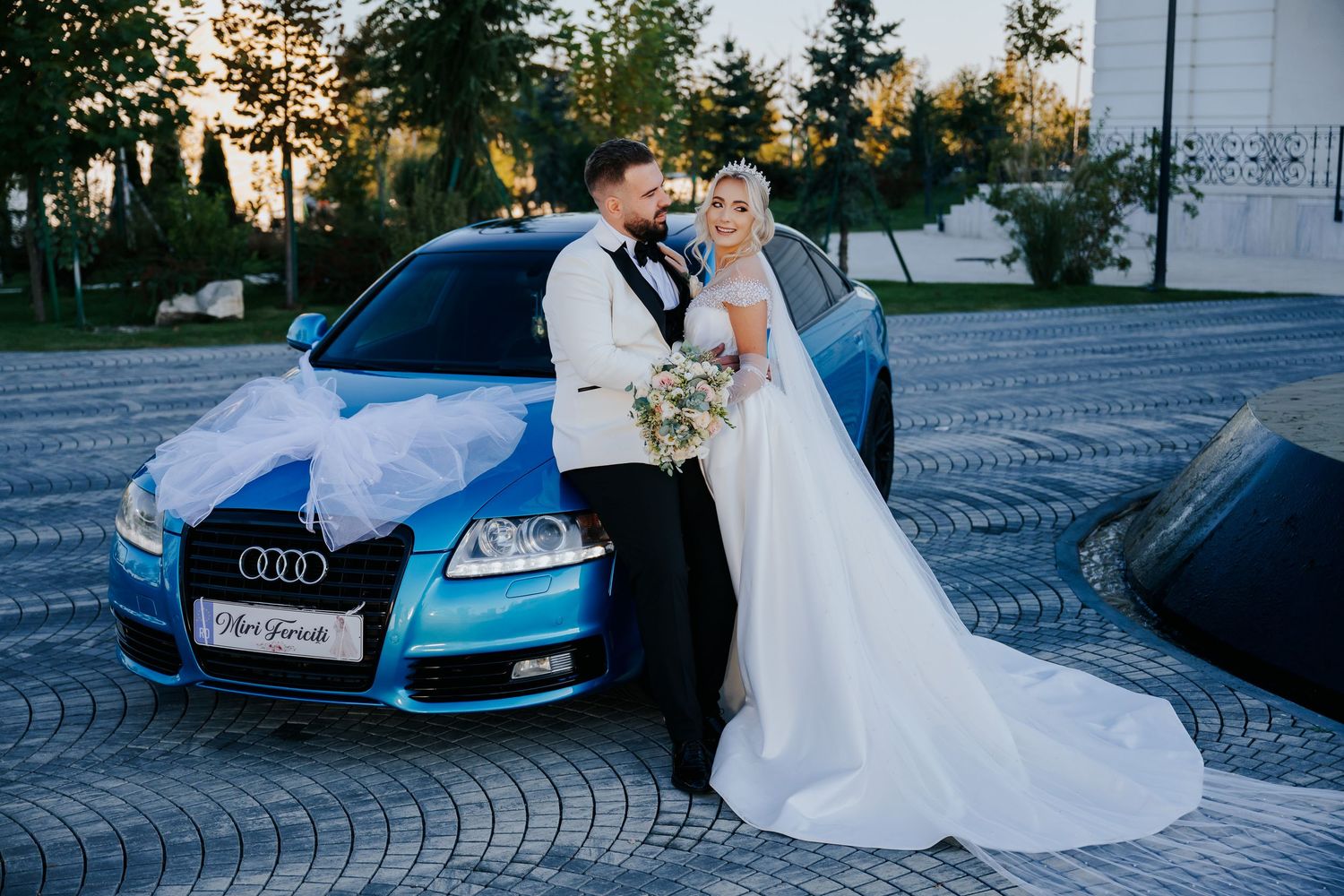 Bride and groom posing together in front of a decorated blue Audi car on their wedding day.