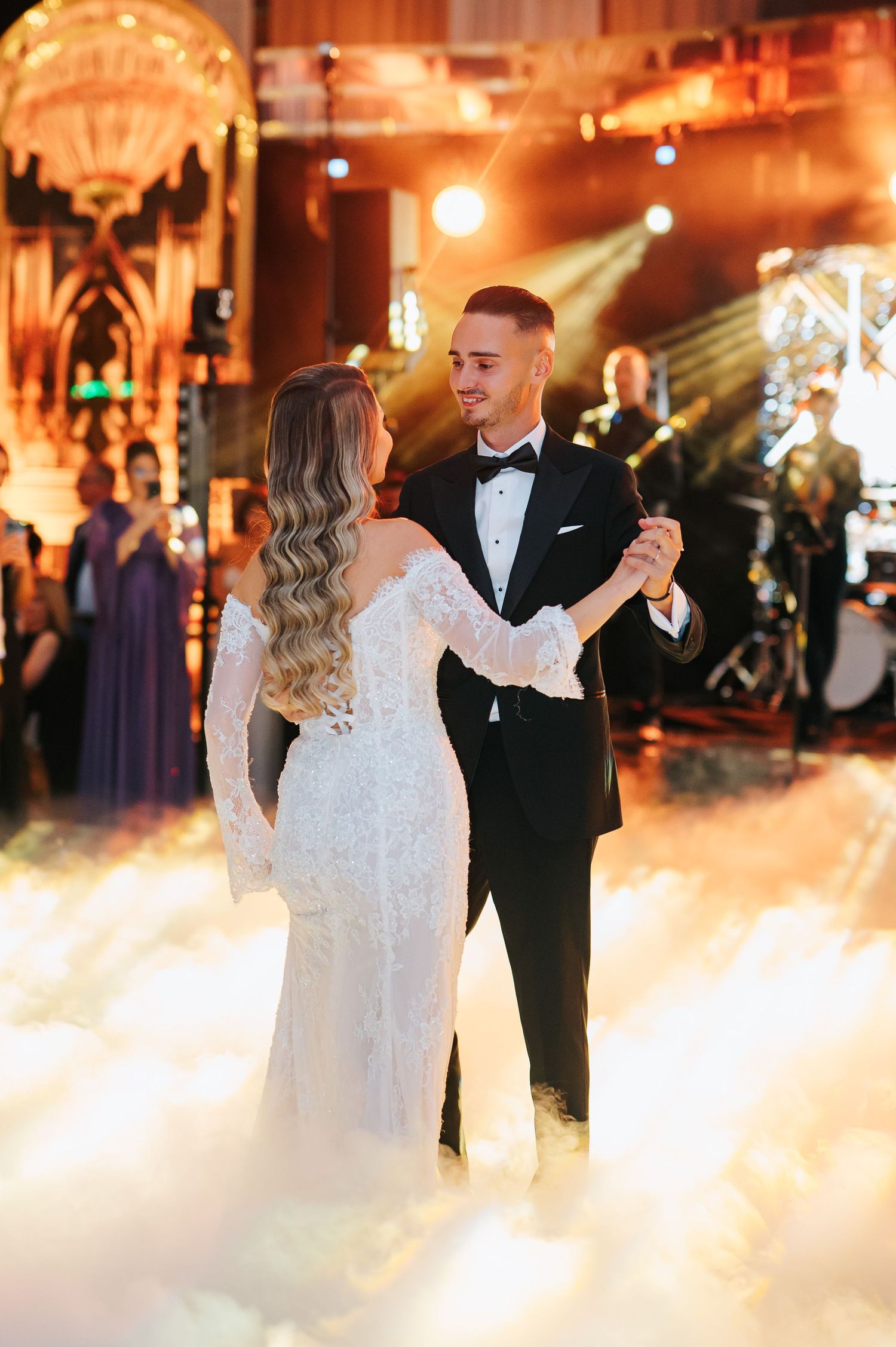 Bride and groom sharing first dance surrounded by dramatic fog on elegant ballroom floor.