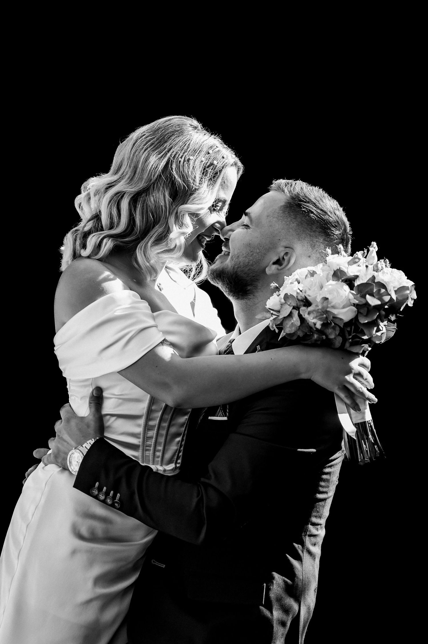 Joyful bride and groom embracing and laughing together in black and white wedding portrait.