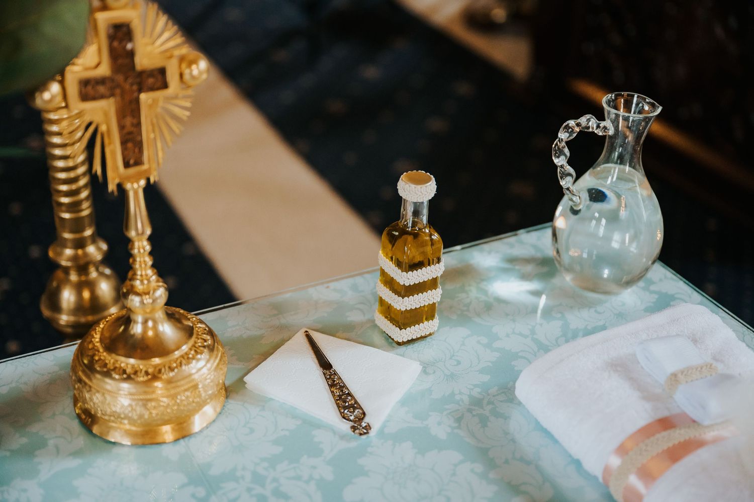 Orthodox Christian altar table with gold cross, holy oil bottle, crystal pitcher, envelope, and white cloth.