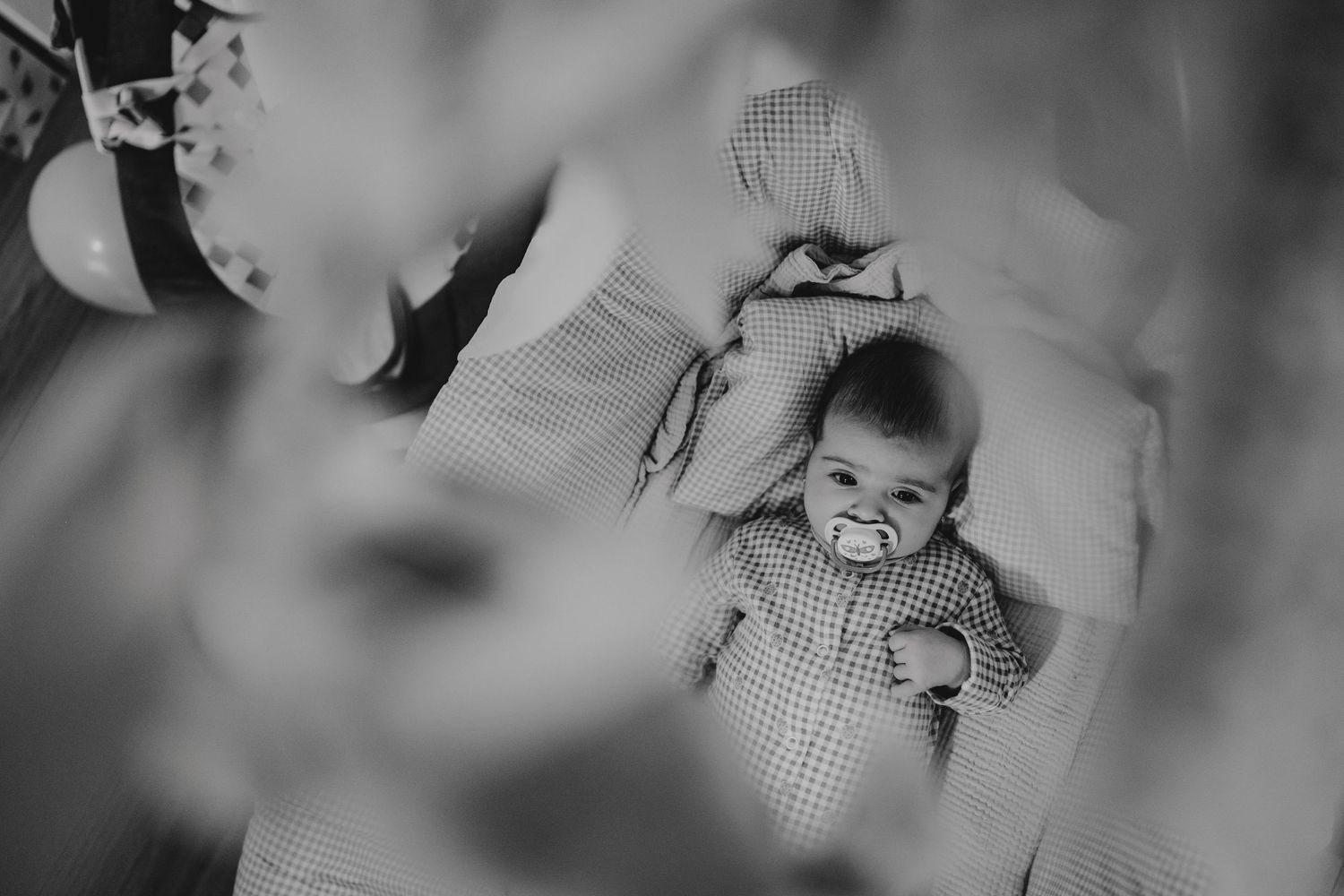 Black and white overhead photo of peaceful baby with pacifier lying on checkered bedding.