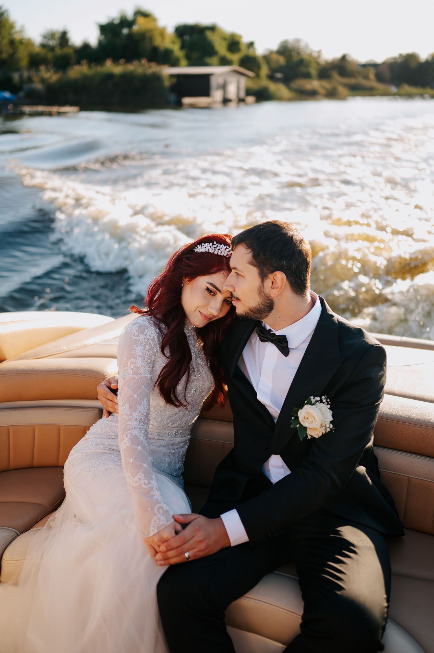 Bride and groom share a romantic moment on a speedboat, with the bride wearing a lace gown and tiara.