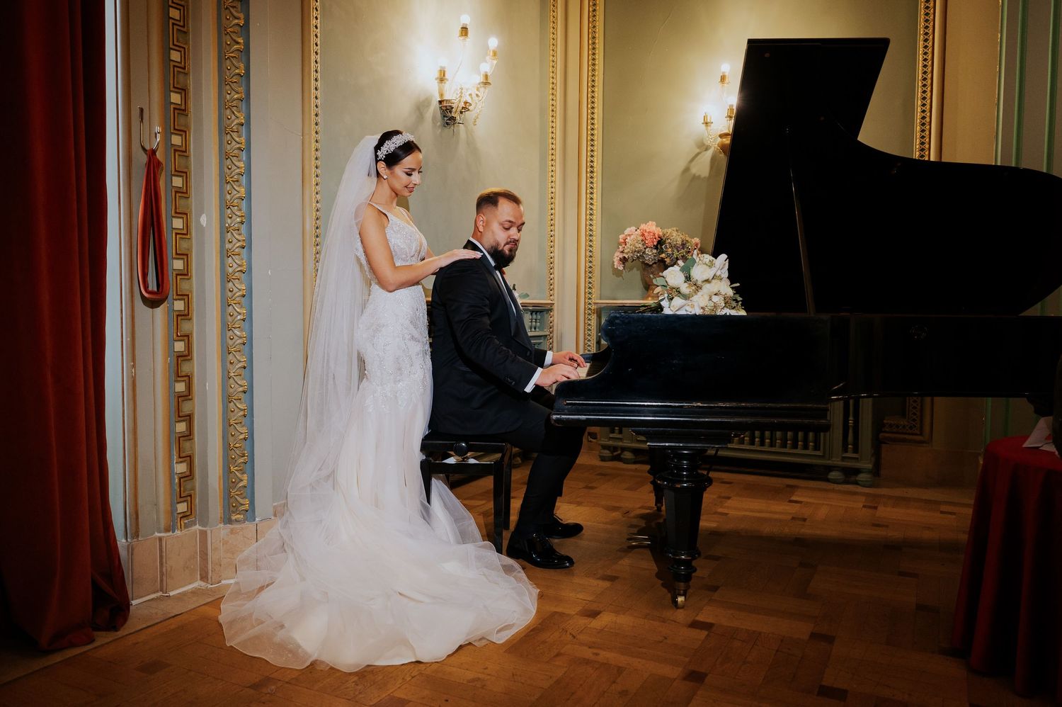 Bride and groom at a grand piano in an elegant ballroom, sharing a romantic wedding moment.