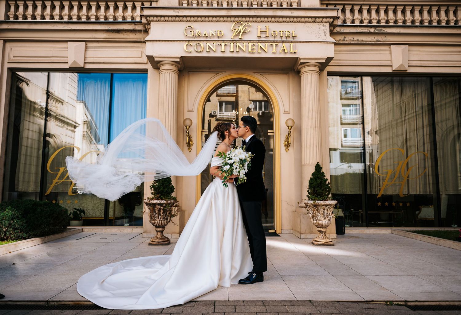 Bride and groom kissing outside the Continental Hotel with veil flowing in the wind.