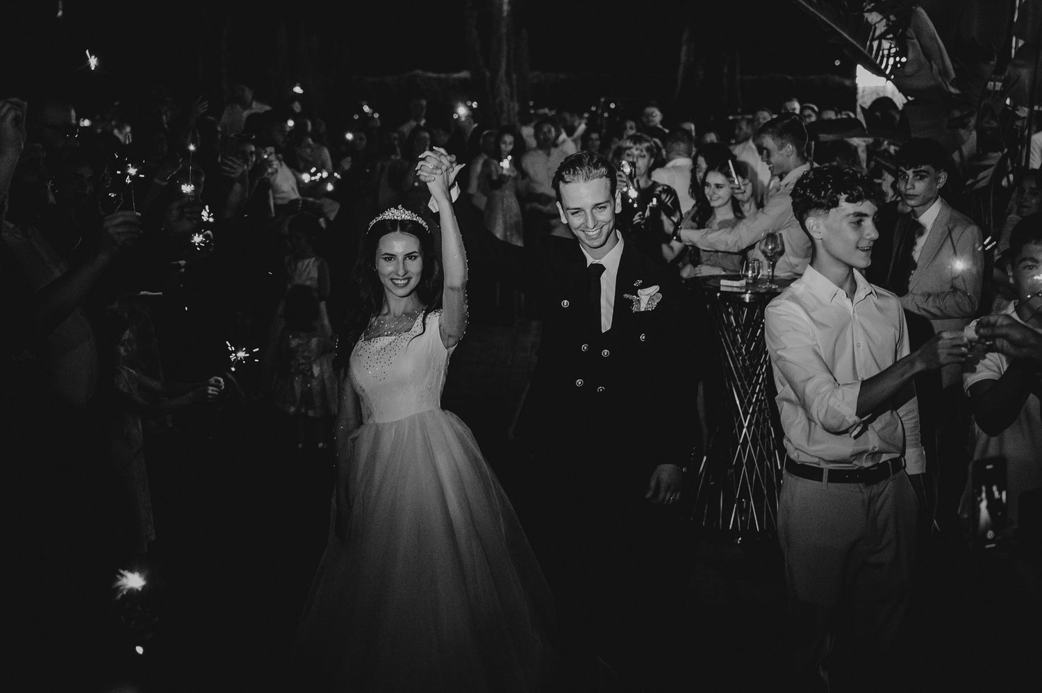 Black and white photo of a joyful bride and groom exiting through a sparkler tunnel at their wedding reception.
