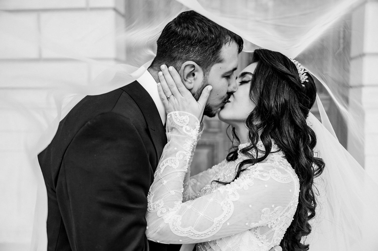 Black and white wedding photo of bride and groom sharing a romantic kiss, bride in lace gown with veil.