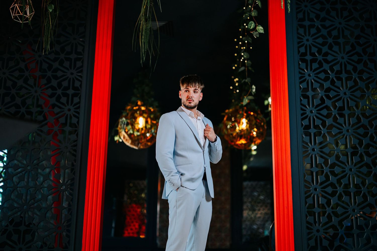 Man in light gray suit standing in elegant venue with red columns and warm ambient lighting.
