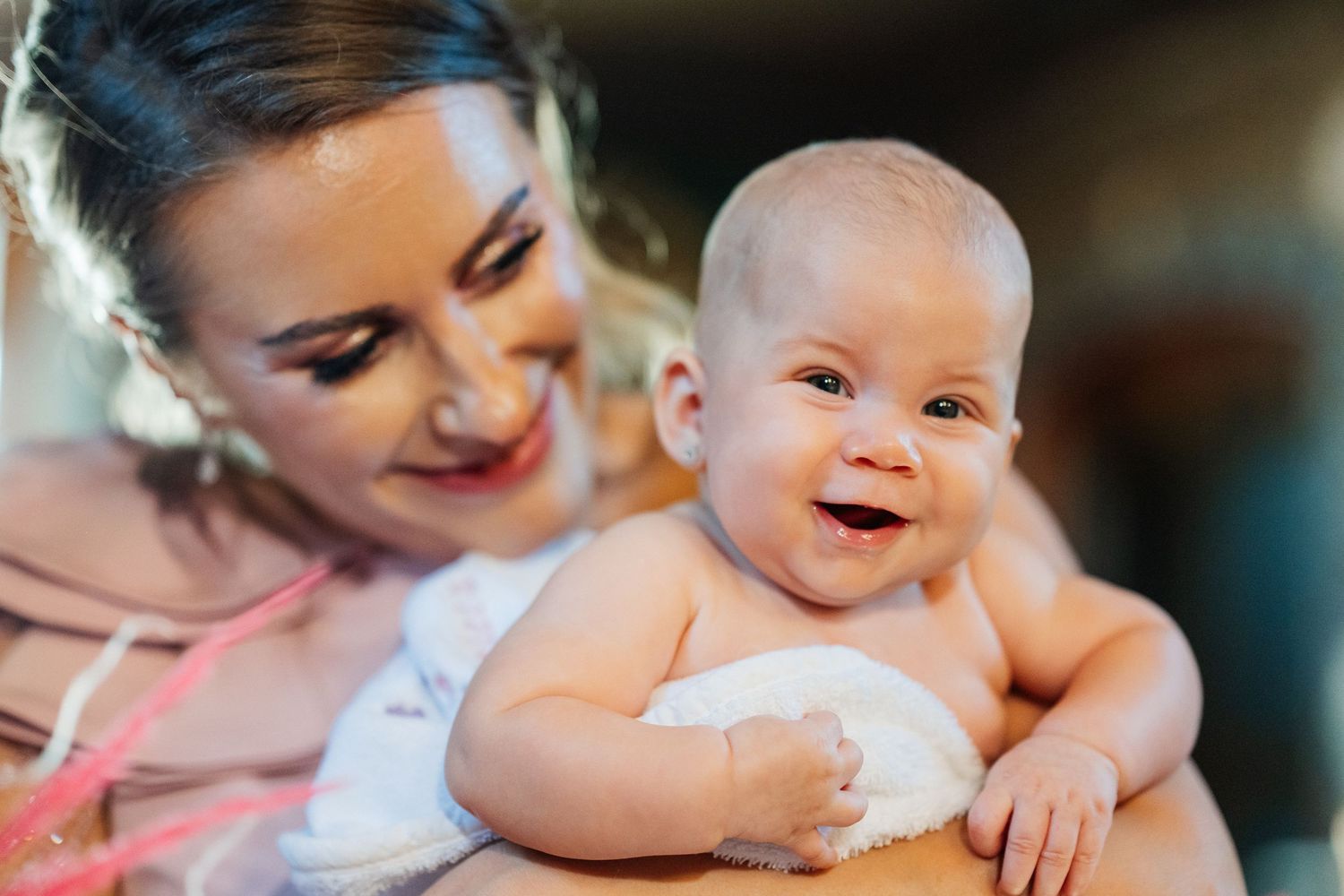 A smiling mother holds her happy, chubby baby close, both sharing a joyful moment together.