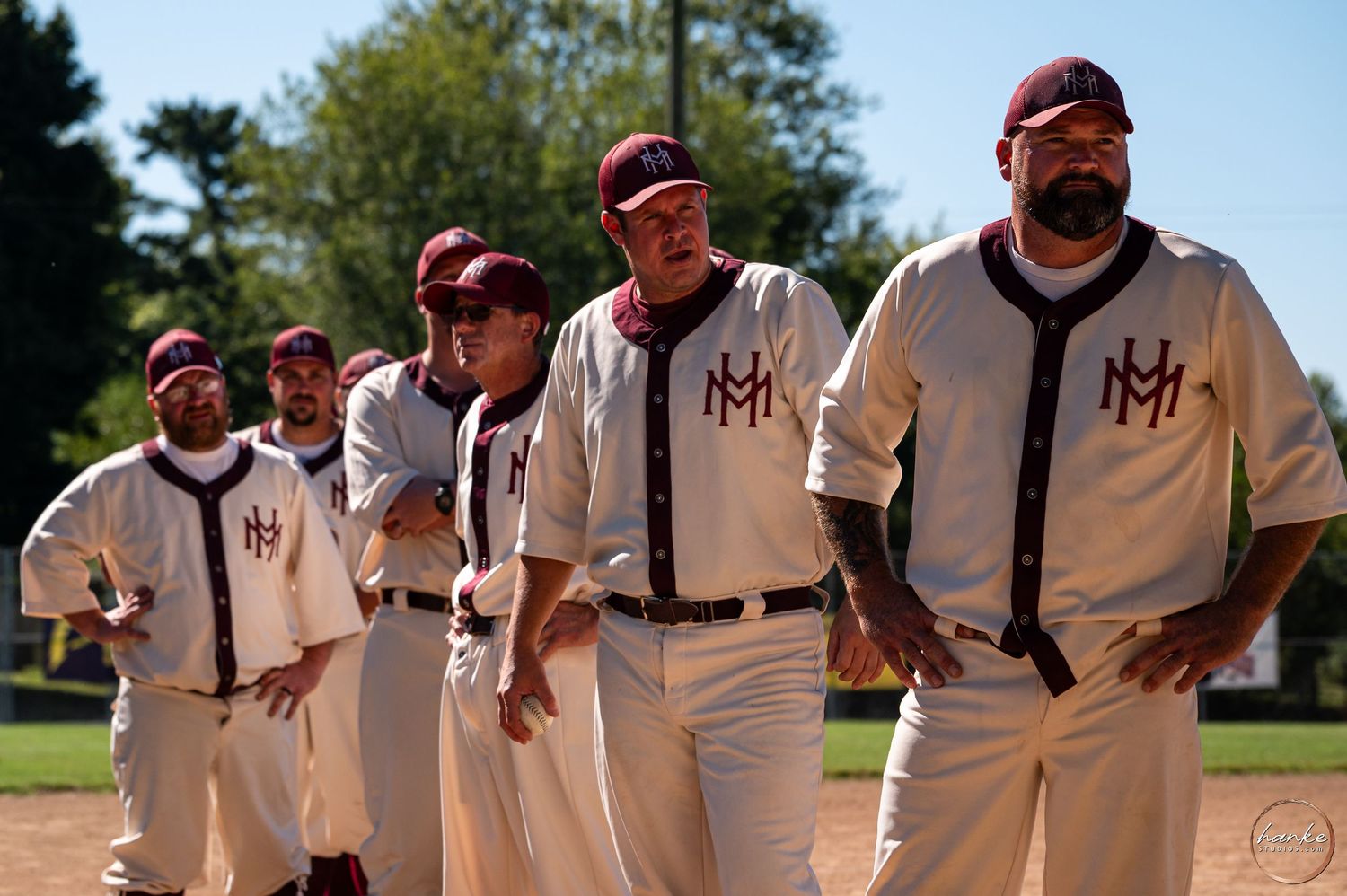 Vintage baseball players in retro MH uniforms walking together on a sunny green field. Mariah Hill Yanks.