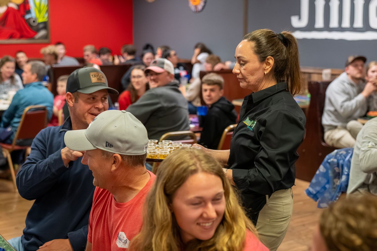 Smiling waitress serves drinks to guests at a busy indoor Cinco de Mayo event.