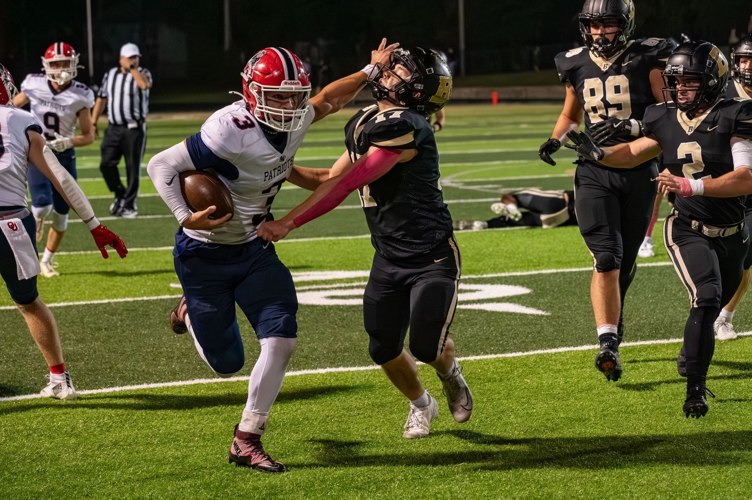 Football player in white jersey stiff-arms defender during night game.