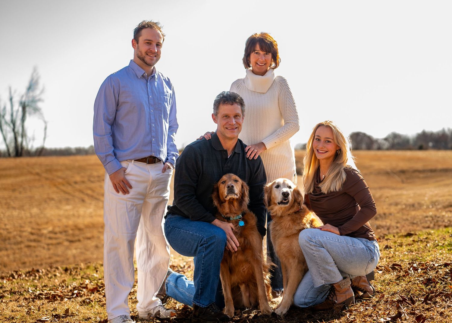 Family portrait with two golden retrievers in an open field during golden hour.