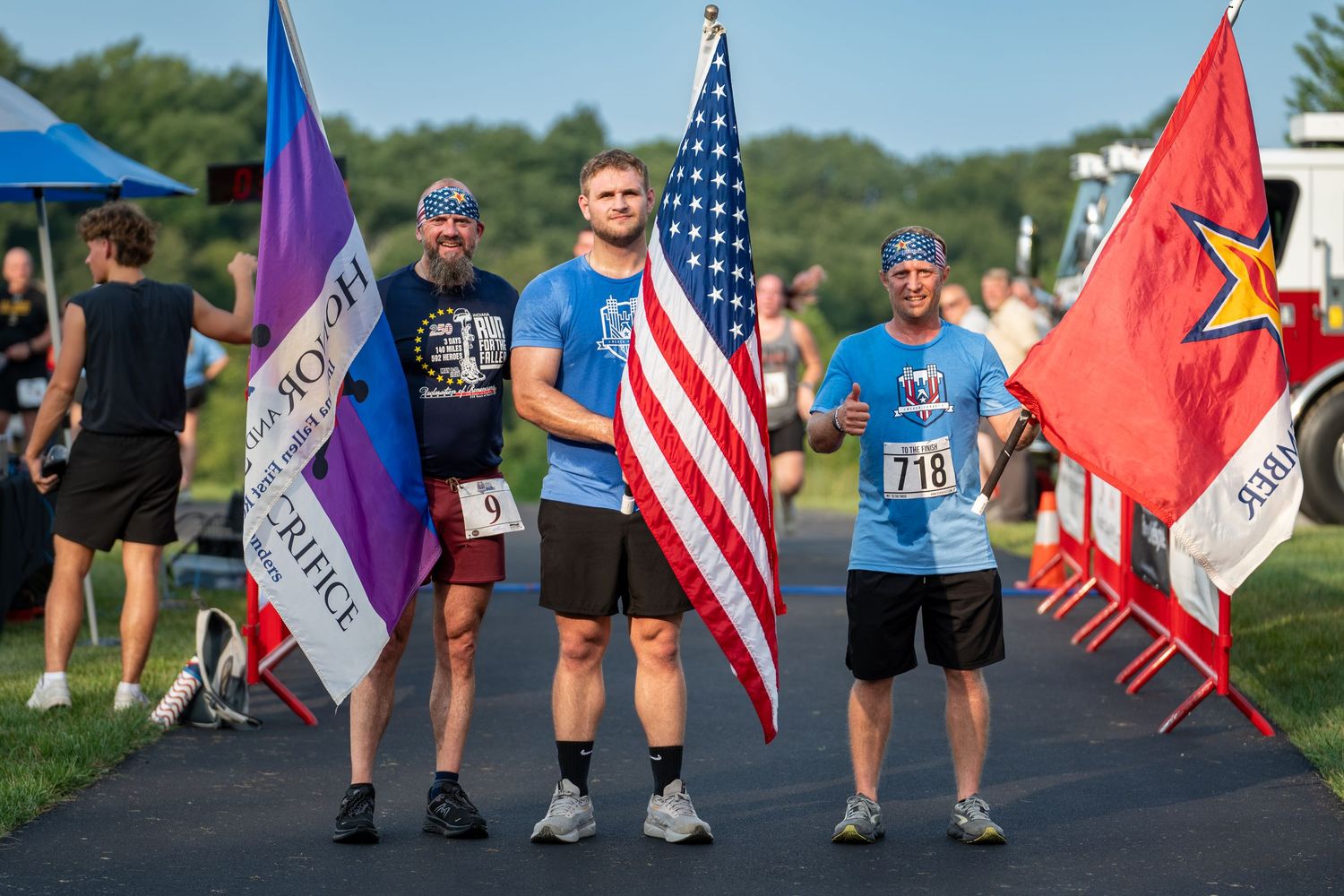 Three runners proudly hold American and military flags at finish line during the 2026 Honor and Remember Run at Cool Springs, OFS Brands