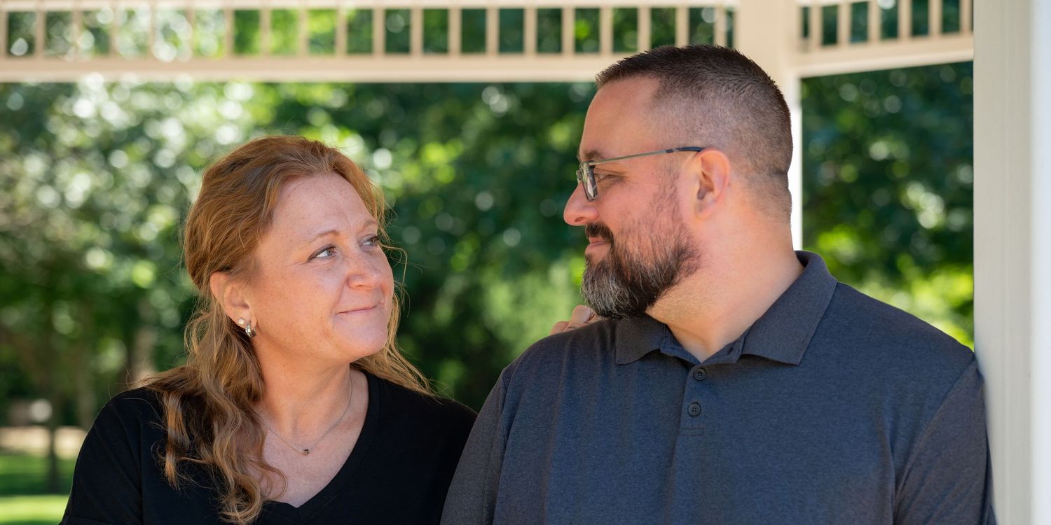 Couple gazing at each other under a white pergola outdoors.