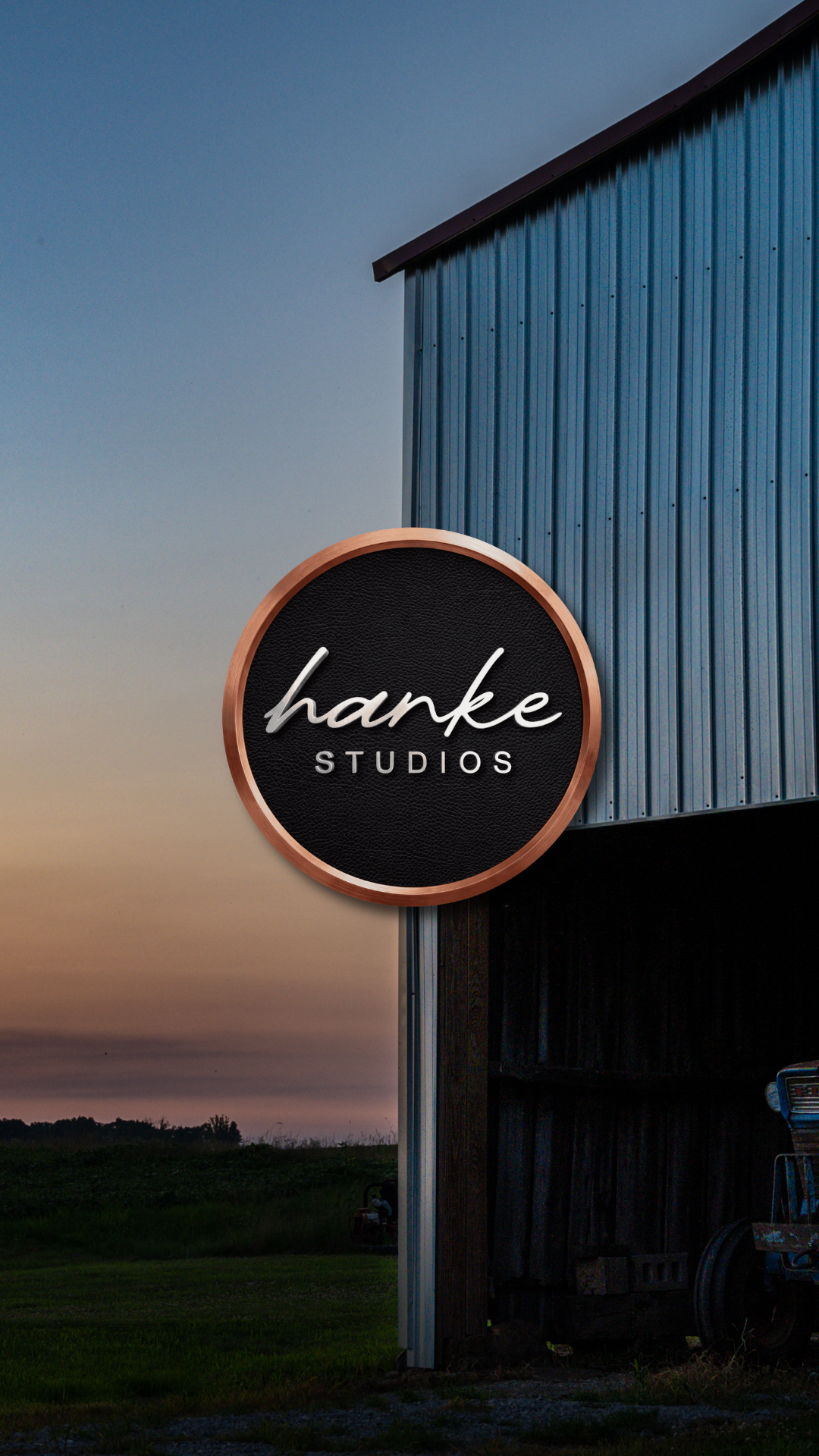 Hanke Studios circular sign mounted on a rustic barn exterior at sunset dusk.