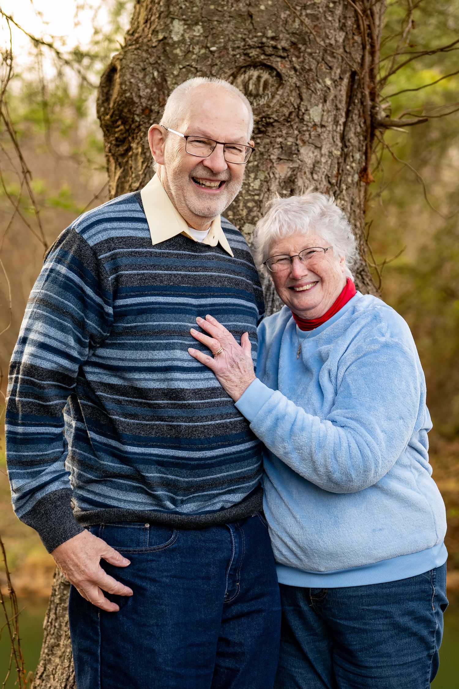Happy senior couple smiles together in front of large tree in autumn outdoor setting.
