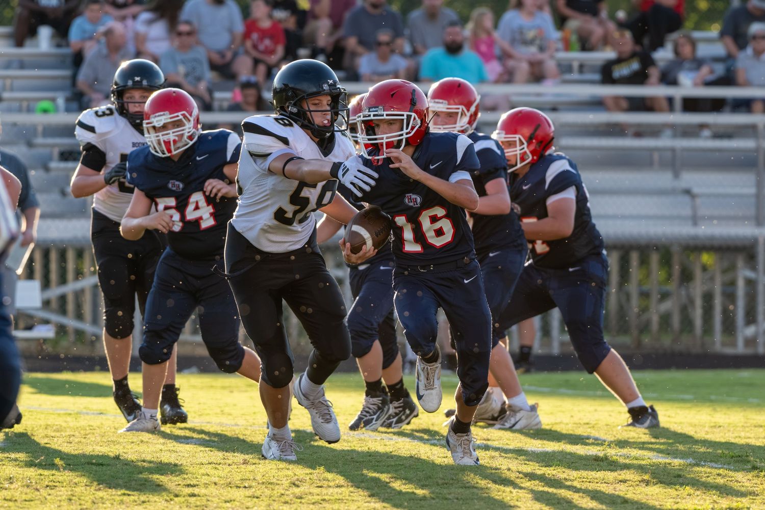 Youth football players in red helmets defend against a ball carrier in a white jersey during a youth football game.