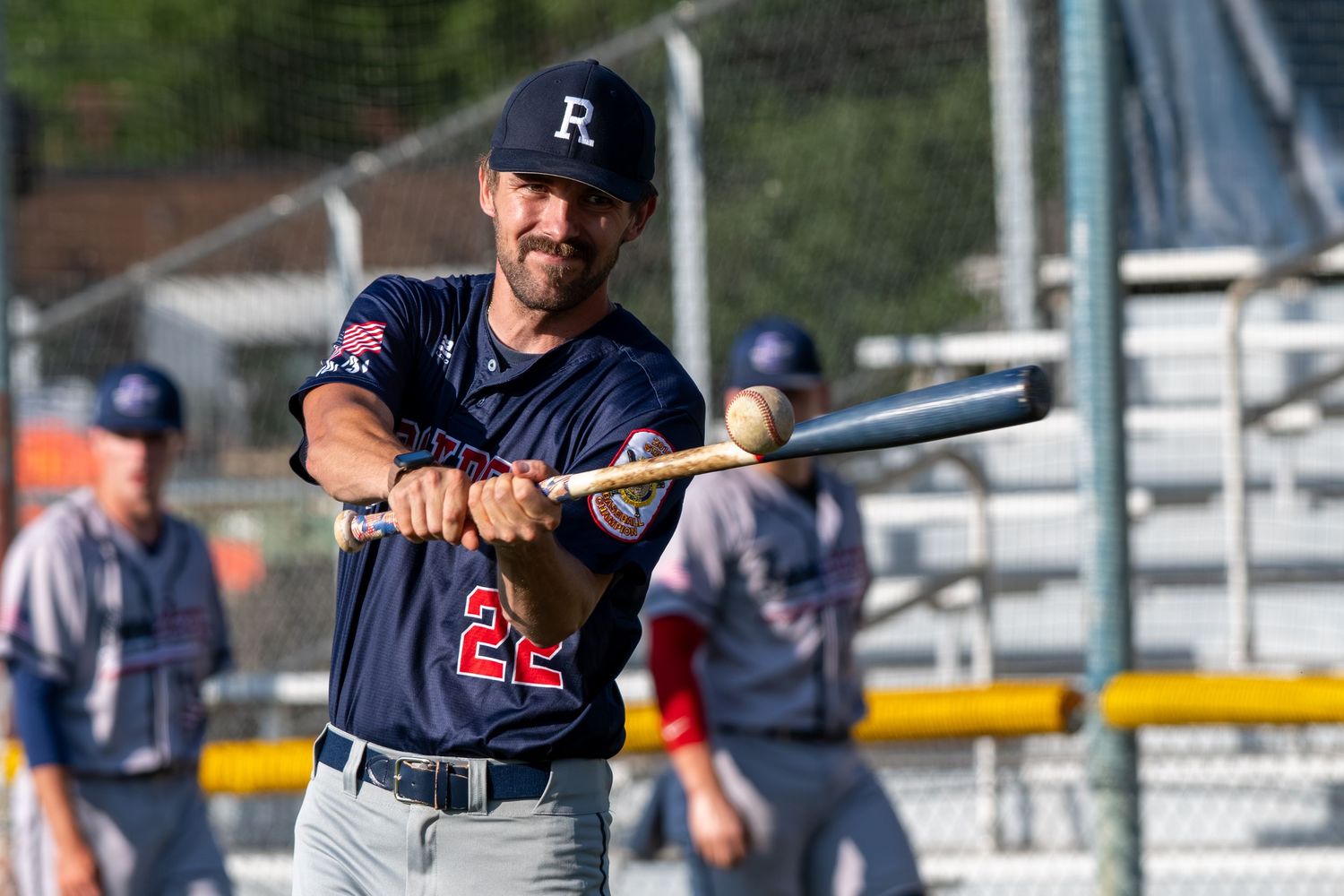 Baseball player wearing number 22 jersey holds bat during warm-up practice at outdoor baseball field.