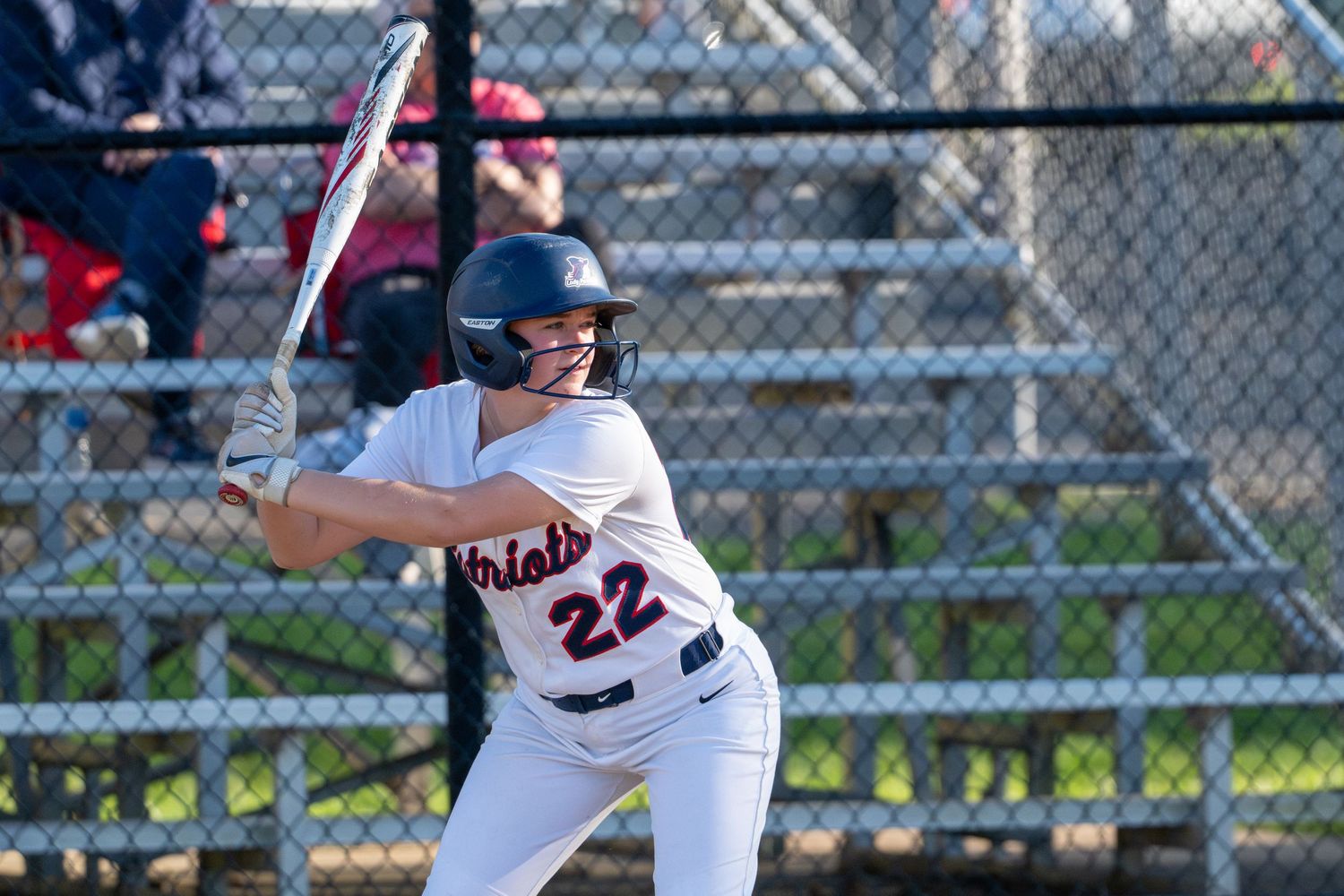 Softball player #22 in white uniform stands ready at bat wearing helmet during a game.