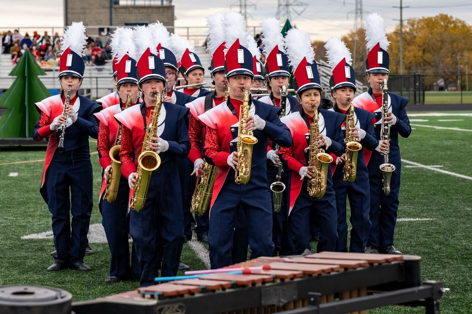 Heritage Hills High school marching band members in red and navy uniforms playing saxophones on a football field.