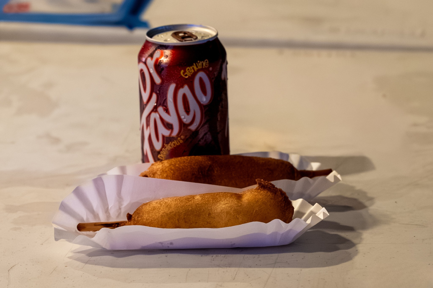 Two corn dogs in a paper tray beside a can of Dr. Pepper on a white surface.