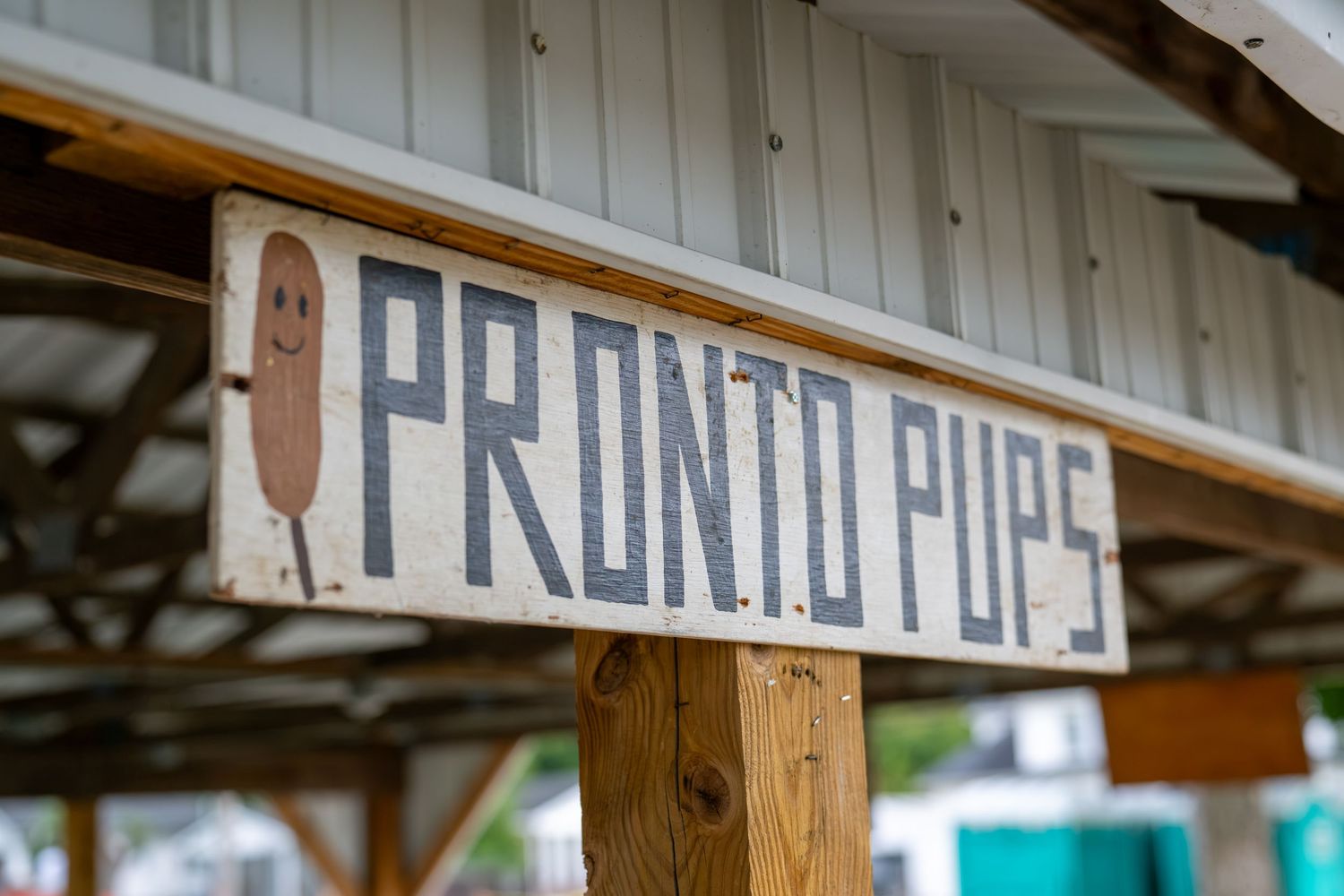 Rustic wooden Pronto Pups sign with corn dog illustration hanging at an outdoor food stand.