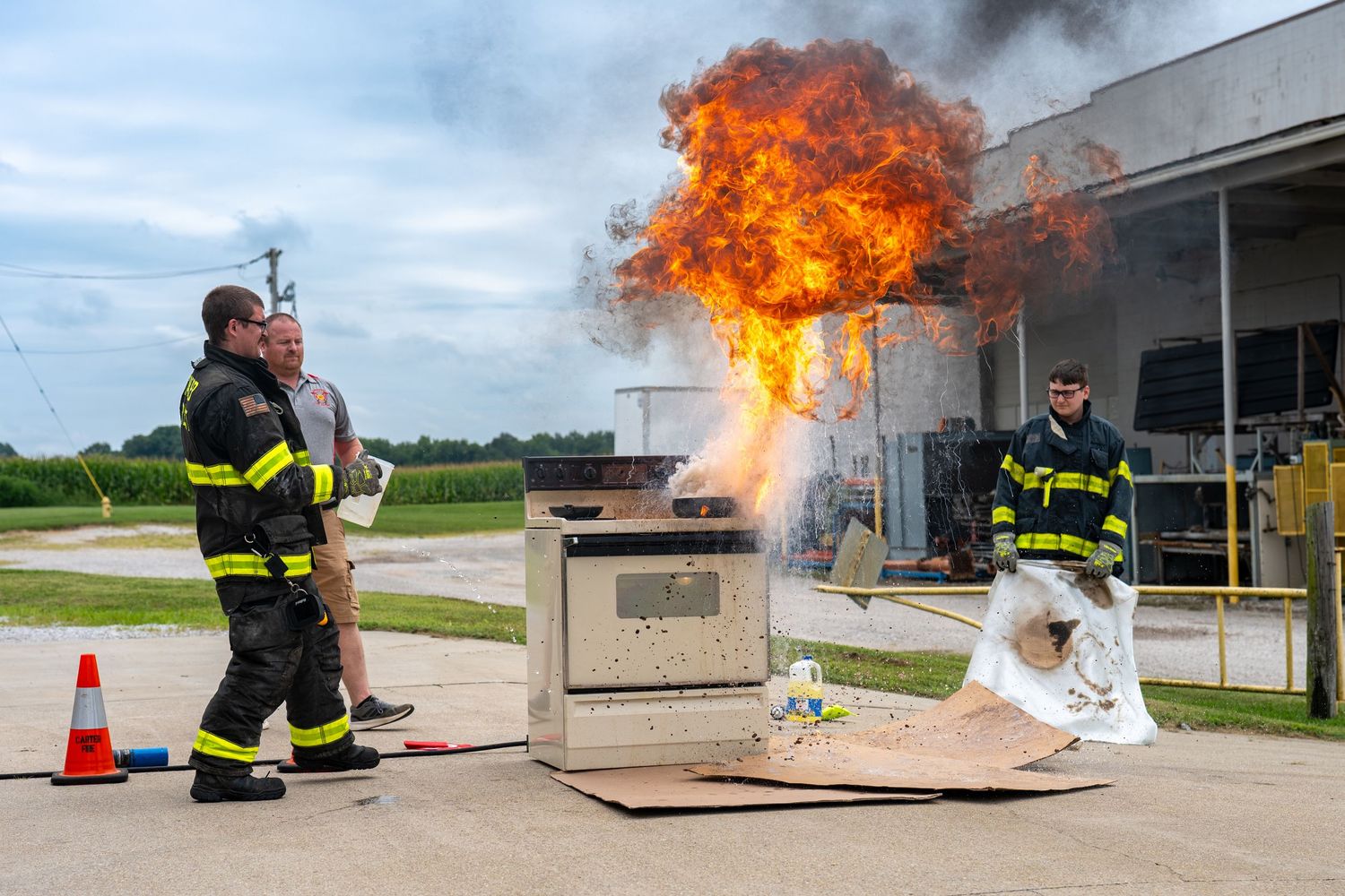 Carter Volunteer Firefighters demonstrating a controlled fire safety training exercise with large flames near a stove outdoors.