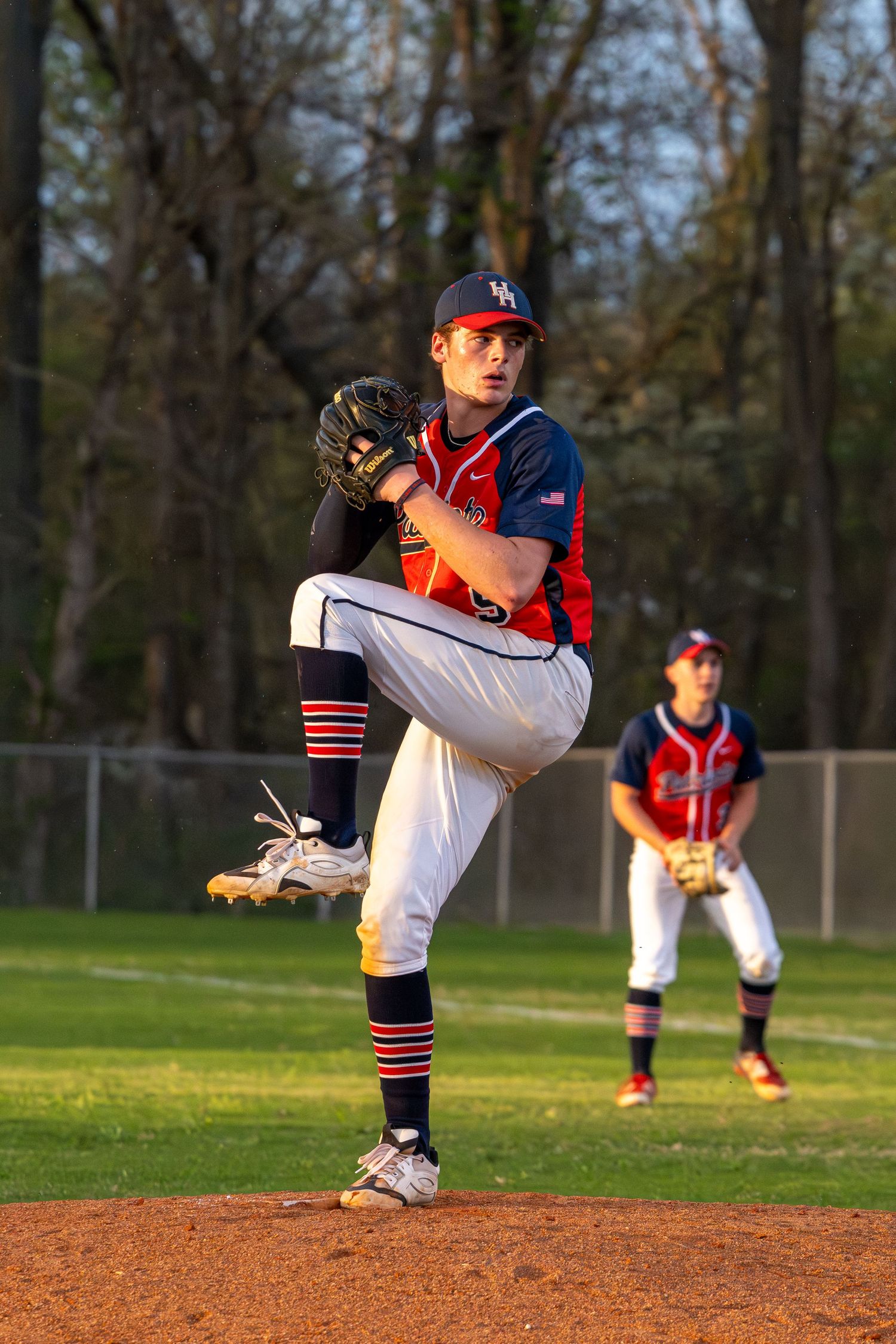 Heritage Hills High school baseball pitcher in red and navy uniform winds up for delivery on pitching mound.