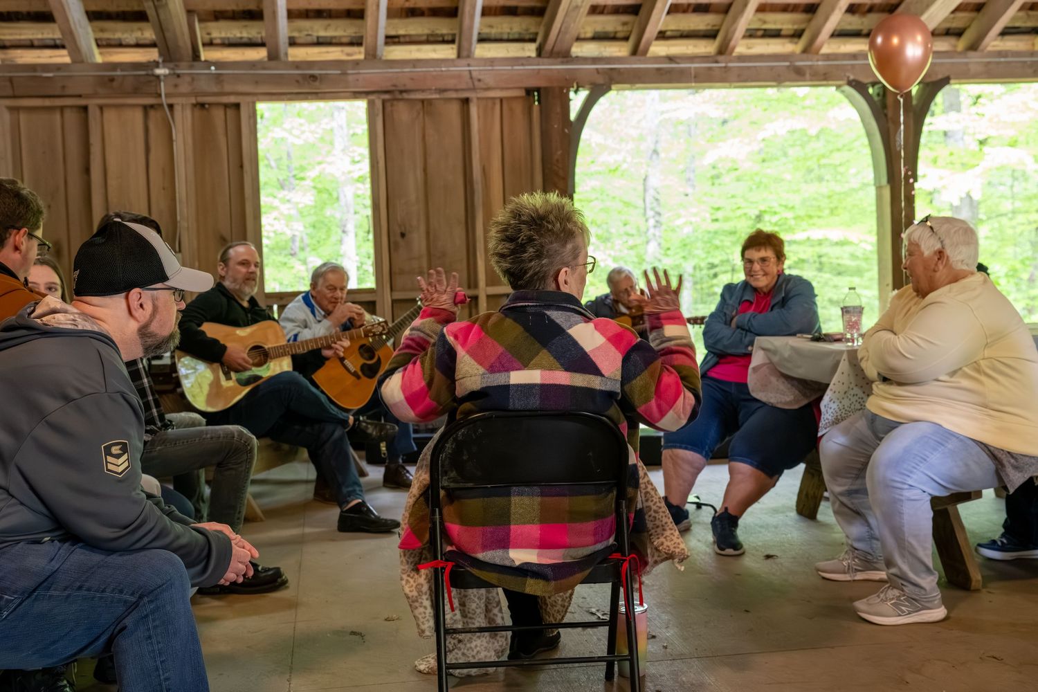 Group of musicians playing guitars and fiddles in a rustic outdoor shelter.