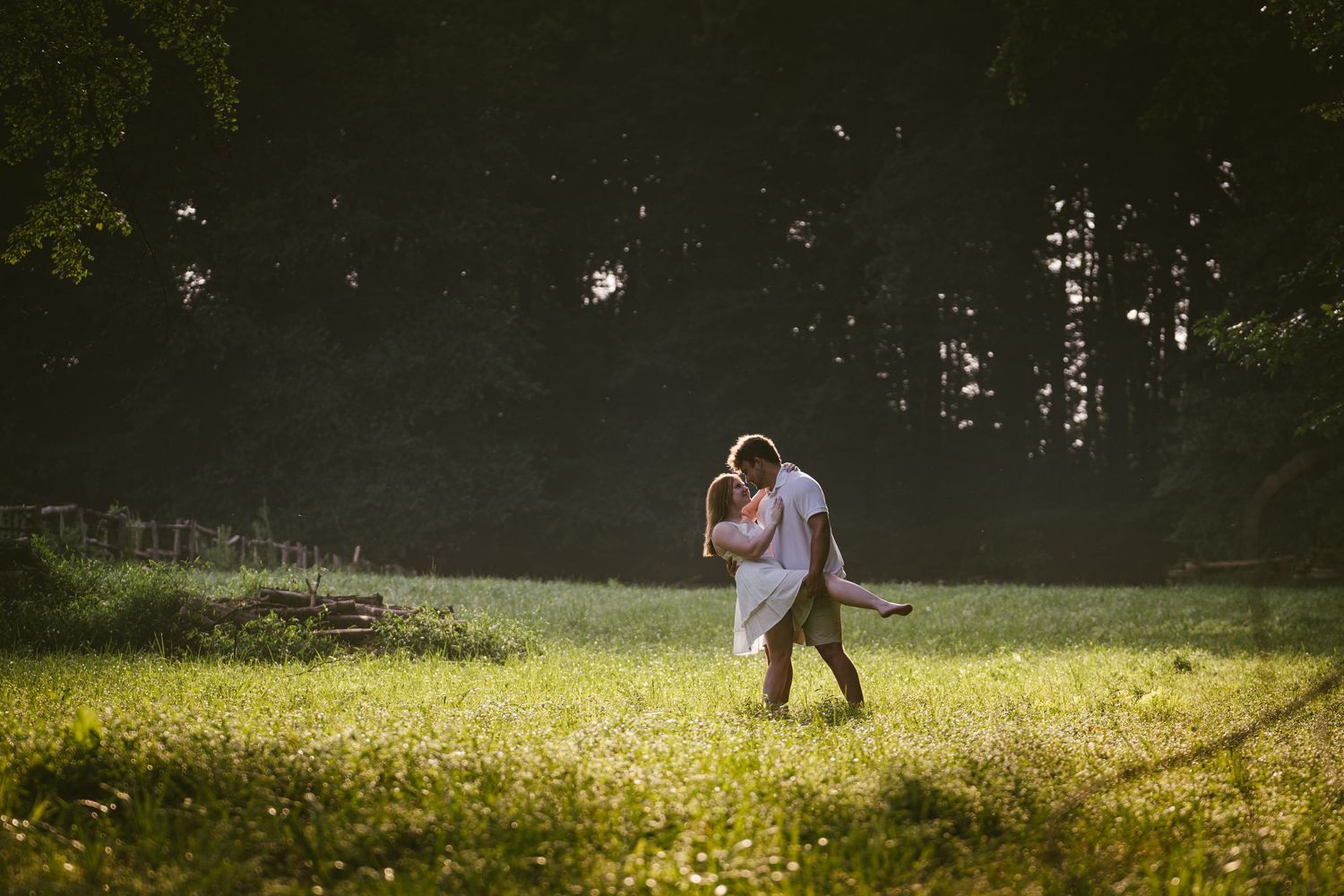 Couple dancing and embracing in a sunlit green meadow with dark forest background.