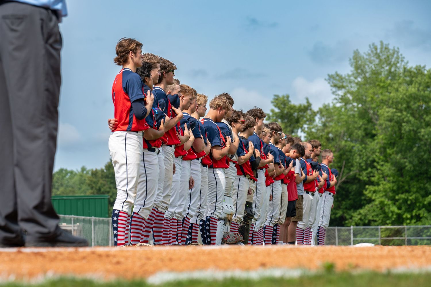 Baseball team lines up along field in red and white uniforms during pre-game ceremony outdoors.