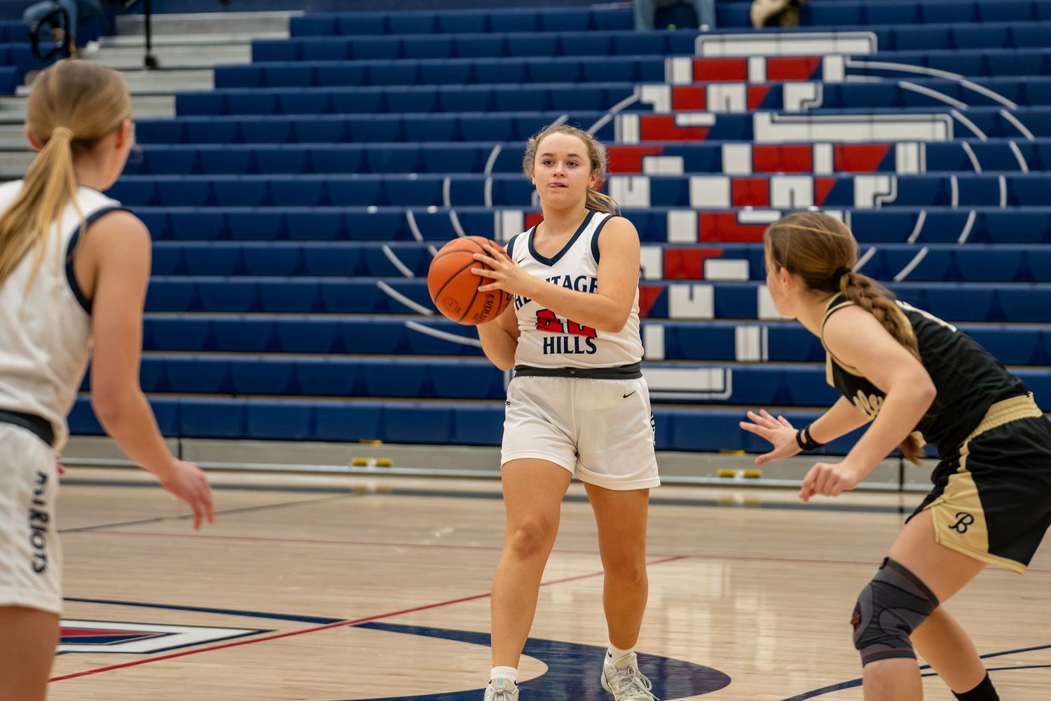 Heritage Hills girls basketball player holds ball during a game, with defenders nearby on a blue court.